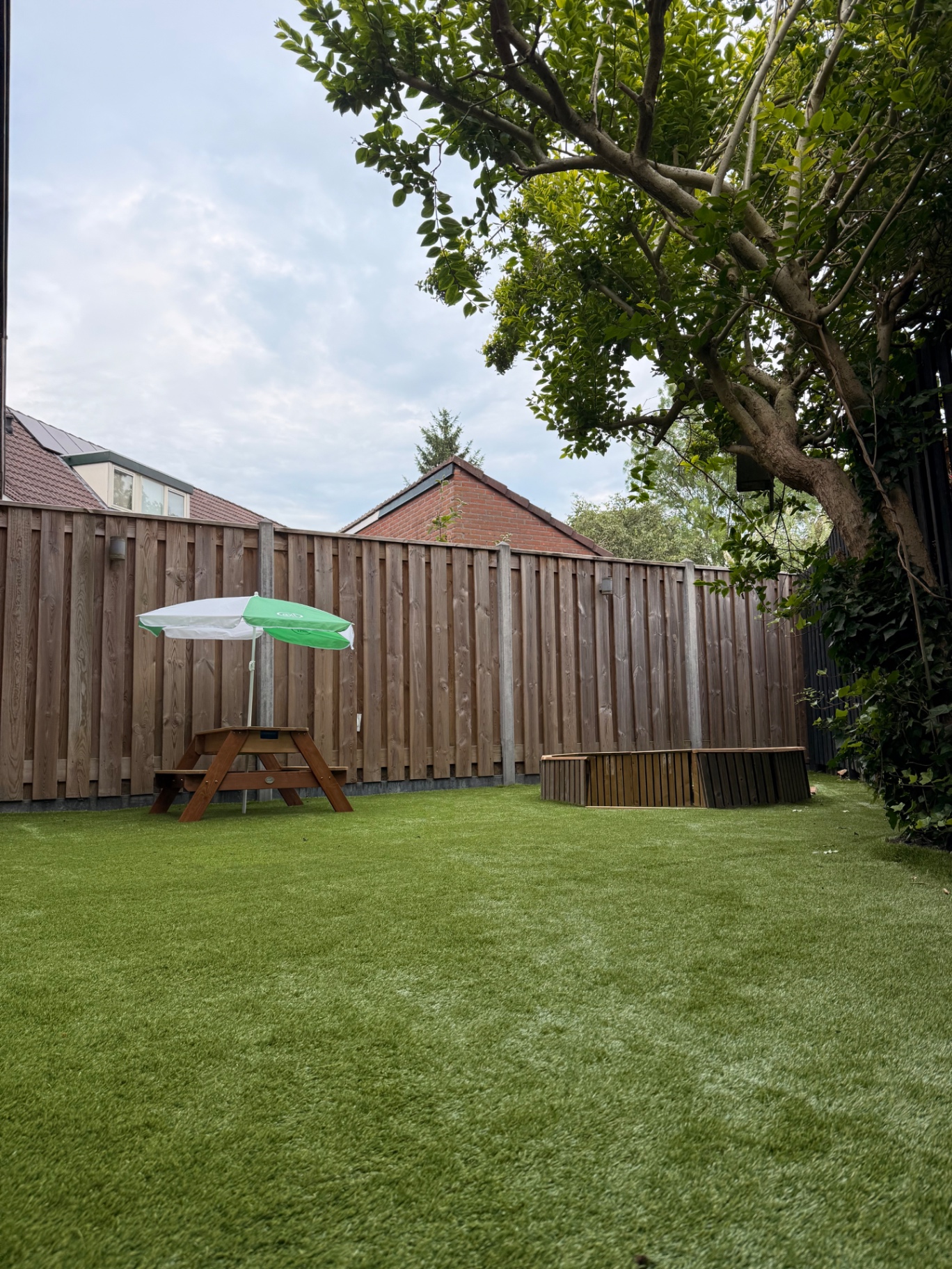 Beschutte achtertuin met kunstgras, picknicktafel en houten speelbak