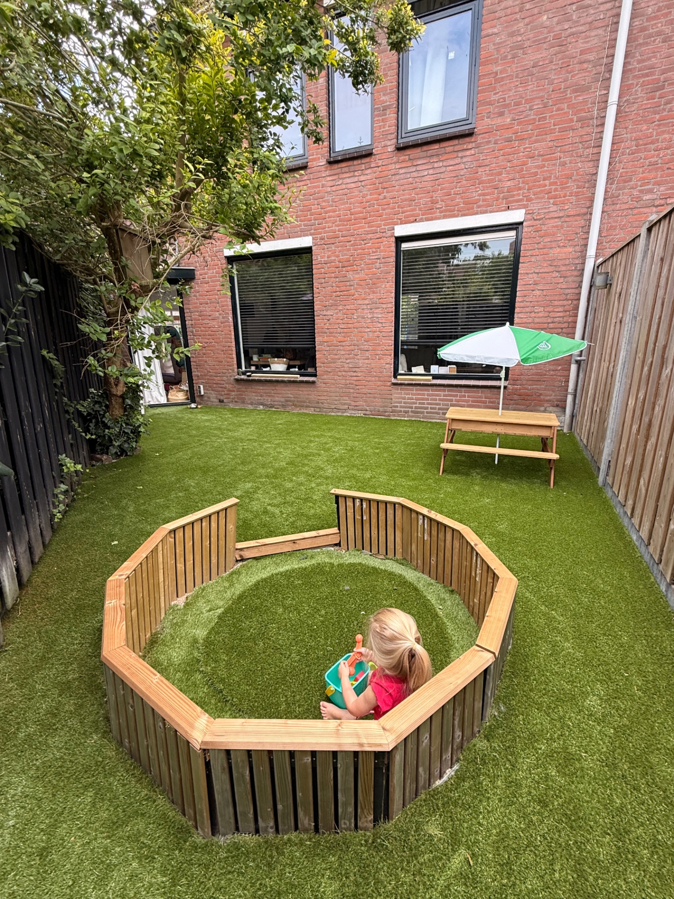 Ronde houten speelbak met kunstgras in de tuin